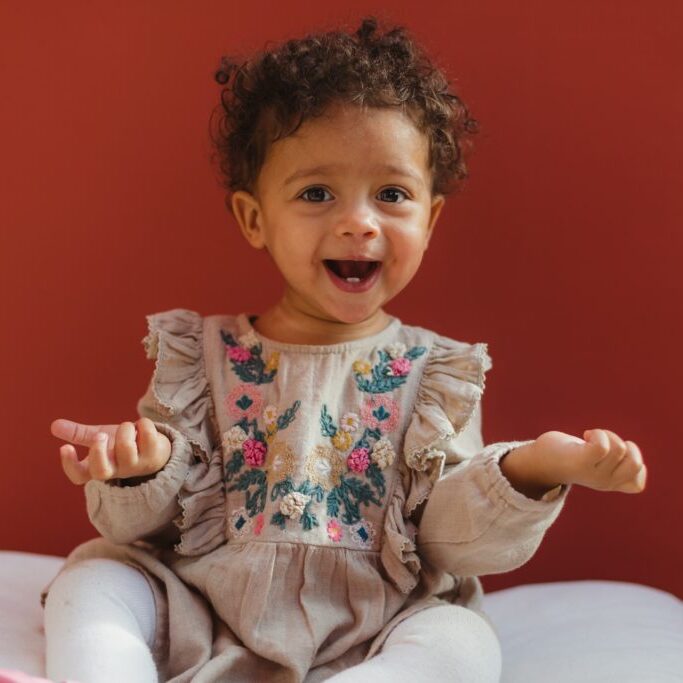 Little girl sitting on pillow in front of red wall